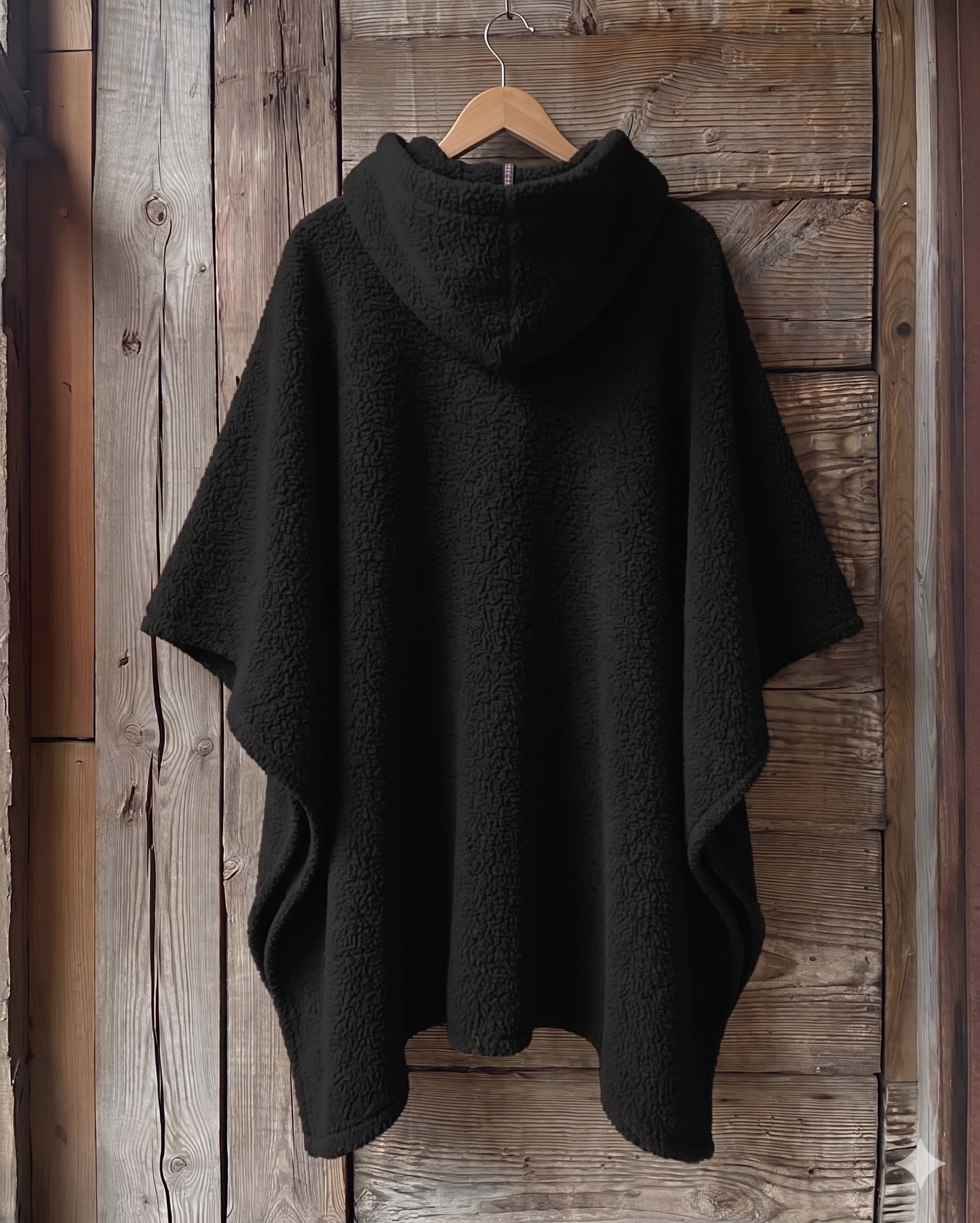 Black oversized hooded fleece cape featuring a large gold Africa-shaped fingerprint graphic on the back, hanging on a wooden hanger against a rustic wooden wall. Modern African-inspired poncho design with a relaxed silhouette and warm texture.